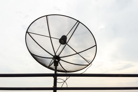 Satellite dish with cloudy sky in background and black fence.