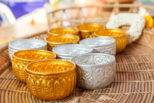 Gold and silver bowl on wooden basket and flower garland in background.