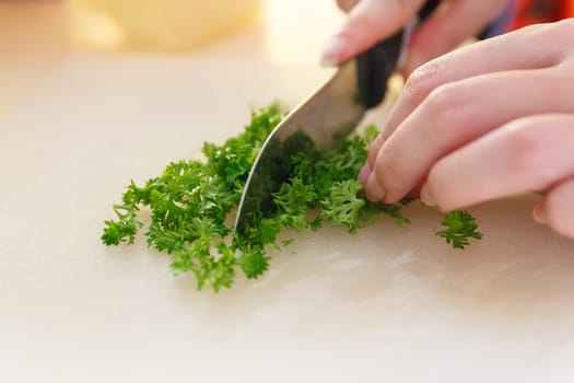 Chef chopping Parsley with knife on plastic board.