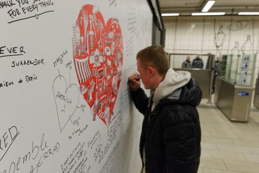 BELGIUM, Brussels : A man writes a message on a commemorative wall at the Maelbeek - Maalbeek metro station on its re-opening day on April 25, 2016 in Brussels, after being closed since the 22 March attacks in the Belgian capital.Maelbeek - Maalbeek metro station was hit by one of the three Islamic State suicide bombers who struck Brussels airport and metro on March 22, killing 32 people and injuring hundreds.