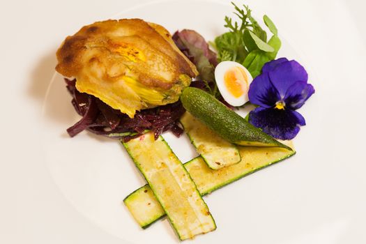 Delicious gourmet plate featuring biscuit sandwich with beets, zucchini strips and pansy garnish over white background