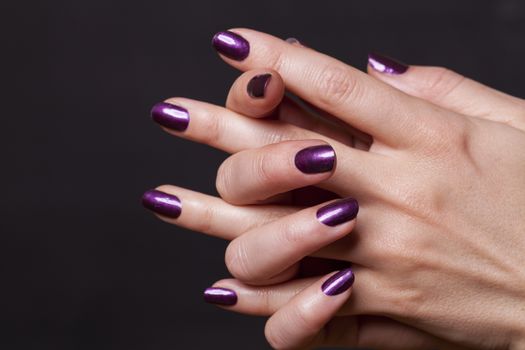 Close up of crossed over female hands decorated with purple fingernail paint over black