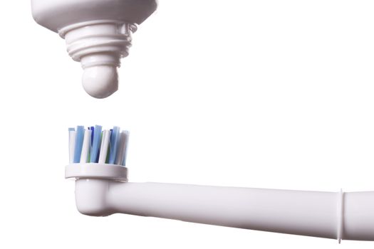 Close up of electric toothbrush with blue bristles and tube with paste bubbled at its opening on white background