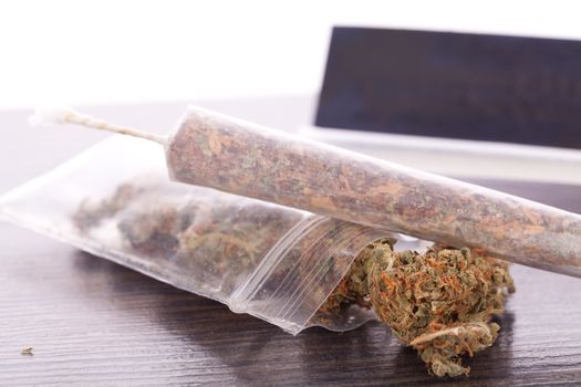 Close up Dried Cannabis Leaves on a Resealable Cellophane Wrapper and a Rolling Paper with Filter on Top of the Table