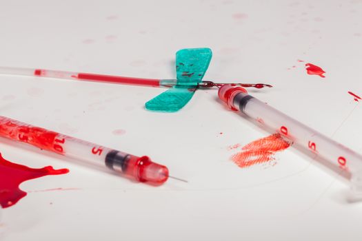 Concept Image - Surgical Aftermath Image of Needle Syringes and IV Lines Covered with Red Blood on White Background in Studio Still Life