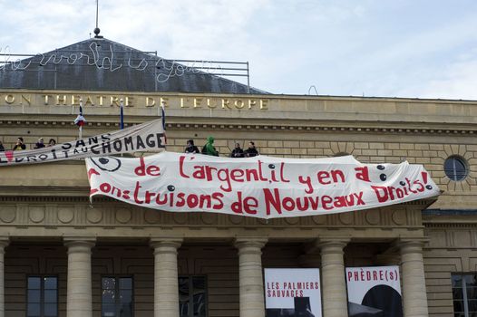 FRANCE, Paris : A man stands by banners reading There is money, let's build new rights displayed on the top of the Odeon theatre as French artists and entertainment workers known in France as intermittents du spectacle occupy the building in Paris on April 25, 2016.Around 50 people occupies the building to protest against the French government's proposed labour reforms and to demand the reshaping of the unemployment insurance before the start of the unemployment insurance negotiations, as part of a protest in conjunction with the Nuit Debout (Night Rising) movement against the French government's proposed labour reforms. 