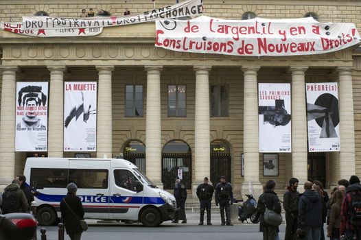 FRANCE, Paris : Policemen stand guard outside the Odeon theatre as French artists and entertainment workers known in France as intermittents du spectacle occupy the building and display a banner reading There is money, let's build new rights in Paris on April 25, 2016.Around 50 people occupied the building to protest against the French government's proposed labour reforms and to demand the reshaping of the unemployment insurance before the start of the unemployment insurance negotiations, as part of a protest in conjunction with the Nuit Debout (Night Rising) movement against the French government's proposed labour reforms. 