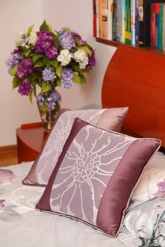 little table with a vase with the flowers and a bed with pillows in a modern bedroom