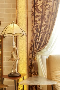 richly decorated curtain with a holding strap at a window in the room near a sofa and a lamp