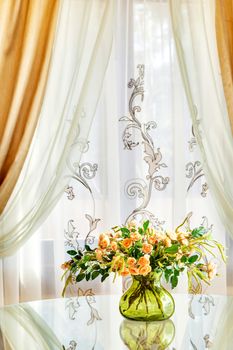 bouquet of roses in a transparent green vase on a table about a window with curtains
