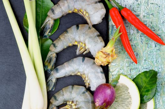 Raw Ingredient of Thai Tom Yam Spicy Soup with Big King Shrimps, Lime, Lemon Grass, Chili Peppers and Ginger closeup on Slate and Wooden background