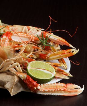 Delicious Grilled Langoustines with Lime and Rosemary on Parchment Paper on White Plate Cross Section on Dark Wooden background
