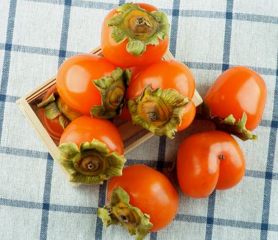 Wooden Box Full of Delicious Raw Persimmon closeup on Checkered Textile Napkin. Top View