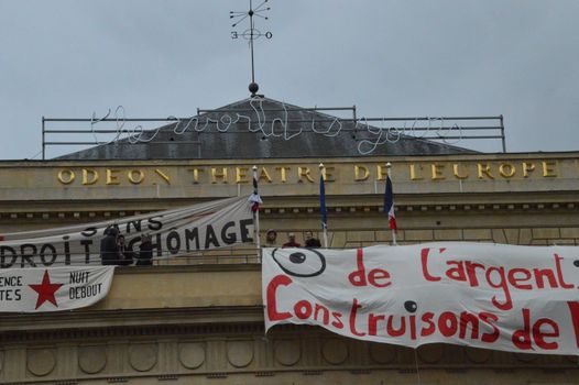 FRANCE, Paris : A man stands by banners reading There is money, let's build new rights displayed on the top of the Odeon theatre as French artists and entertainment workers known in France as intermittents du spectacle occupy the building in Paris on April 25, 2016. Around 50 people occupies the building to protest against the French government's proposed labour reforms and to demand the reshaping of the unemployment insurance before the start of the unemployment insurance negotiations, as part of a protest in conjunction with the Nuit Debout (Night Rising) movement against the French government's proposed labour reforms.