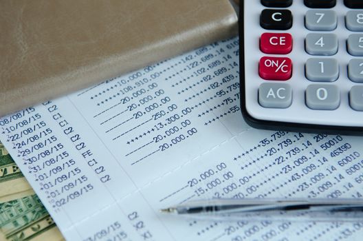 Calculator and pen on bank account passbook with dollar banknote, selective focus