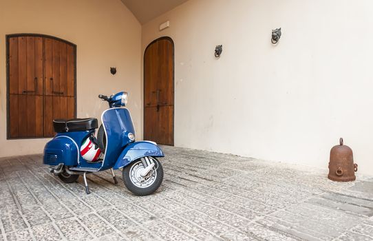 Red scooter Vespa parked by the wall in an italian courtyard