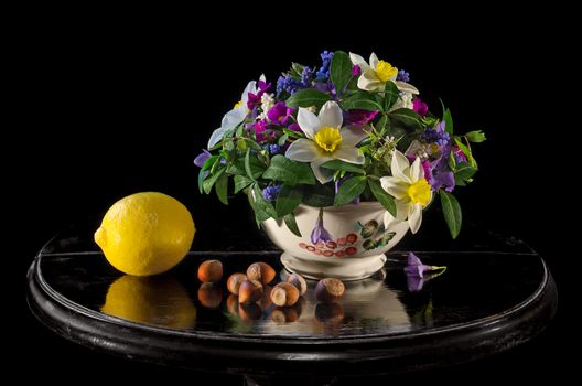 Lemon, hazelnuts and a bouquet of spring flowers, on a black background and antique black table from wood