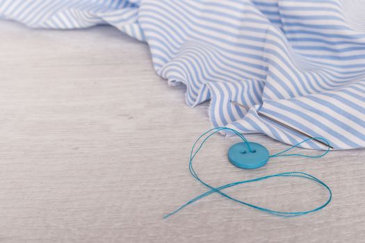 Button, thread and needle on the piece of fabric over rustic wooden table. Top view with copy space.