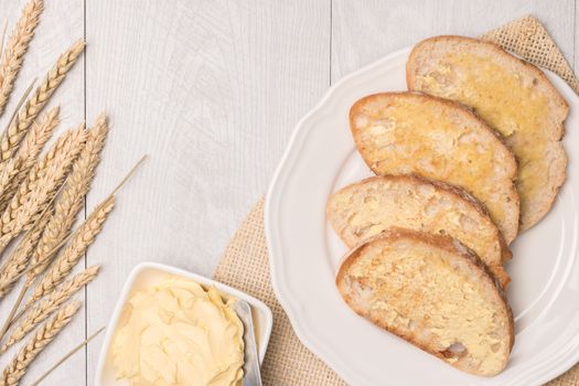 Fresh bread, wheat spike and homemade butter on wooden background. Top view with copy space.