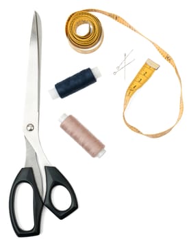 Tailors tools - scissors, spool of thread and tape measure on white. Top view