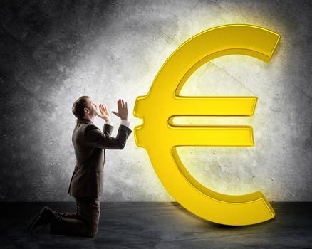 Businessman on knees in front of euro sign on grey wall background