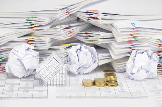 Bankruptcy of house with step pile of tumbledown gold coins on finance account have blur paper ball and pile of paperwork with colorful paperclip as background.