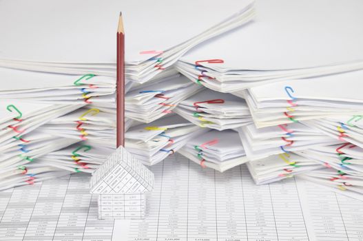 House on finance account have blur brown pencil place vertical behind house and overload of paperwork with colorful paperclip as background.