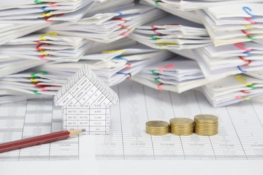 Brown pencil and house with step pile of gold coins on finance account have blur  overload of paperwork with colorful paperclip as background.