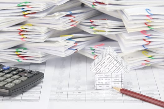 House with brown pencil and calculator on finance account have blur overload of paperwork with colorful paperclip as background.