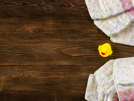 Japanese disposable diapers and the rubber duckling on dark wooden background with copy-space. Flat lay