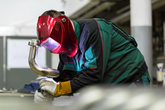 Industrial worker with protective mask welding inox elements in steel structures manufacture workshop.