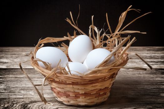 white chicken eggs in a wicker basket closeup on dark table
