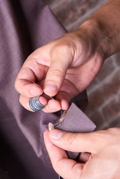 The dressmaker sews a button on a jacket