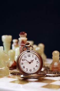 Vintage pocket watch on chessboard against dark background