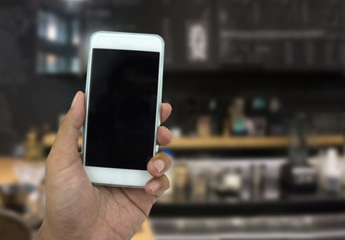 Hand holding smart phone over blured background of coffee shop