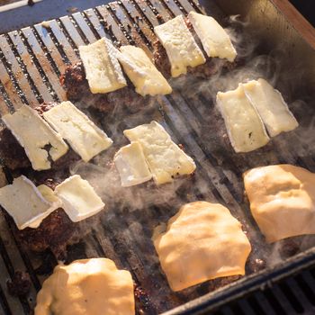 Beef burgers being grilled on food stall grill on international street food festival event. 