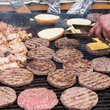 Chef making beef burgers outdoor on open kitchen international food festival event. Street food ready to serve on a food stall.