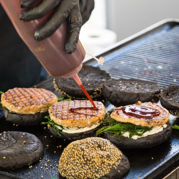 Chef making beef burgers outdoor on open kitchen international food festival event. Street food ready to serve on a food stall.