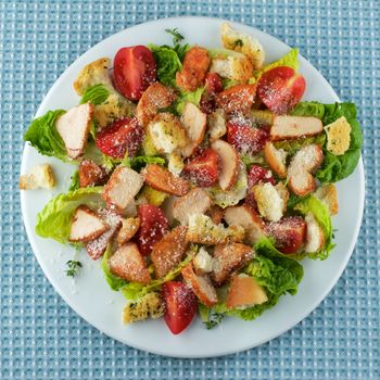 Delicious Caesar Salad with Roasted Chicken Breast, Garlic Crouton, Romaine Lettuce, Cherry Tomatoes and Grated Parmesan Cheese closeup on White Plate. Top View on Blue Napkin
