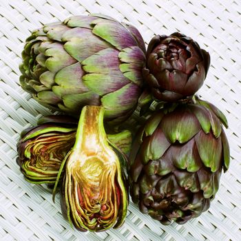 Heap of Perfect Raw Artichokes Full Body and Halves closeup on Wicker background. Top View