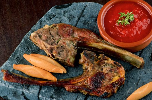 Delicious Roasted Lamb Ribs with Bread Sticks and Tomato Sauce closeup on Stone Plate