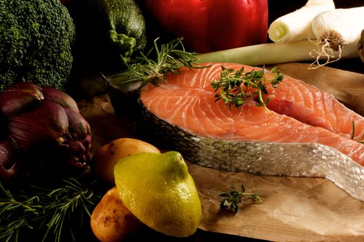 Perfect Raw Steak of Salmon with Raw Vegetables, Greens and Lemon closeup on Wooden Cutting Board