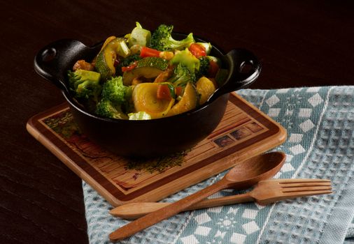 Delicious Homemade Colorful Vegetables Ragout with Zucchini, Carrots, Broccoli, Leek and Red Bell Pepper in Black Iron Stewpot with Wooden Spoon and Fork closeup on Blue Napkin