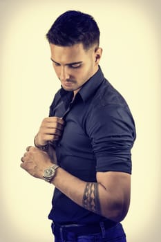 Handsome young man in blue shirt and jeans posing on light background in studio, looking down