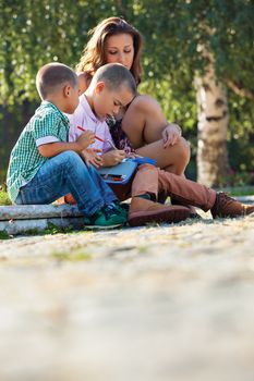 Back to school - two little boys studying lesons in the summer or spring park with their mother.