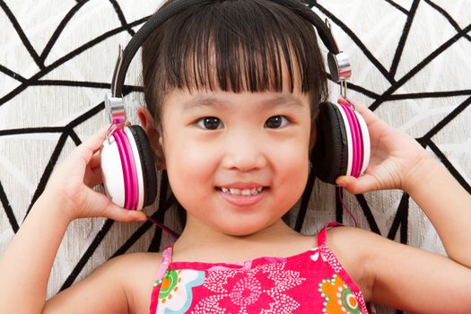 Chinese little girl on headphones holding mobile phone sitting on sofa