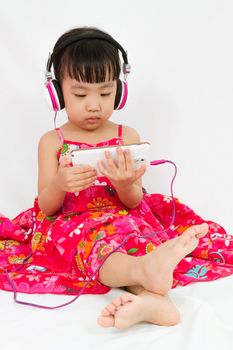 Chinese little girl on headphones holding mobile phone in plain isolated white background.