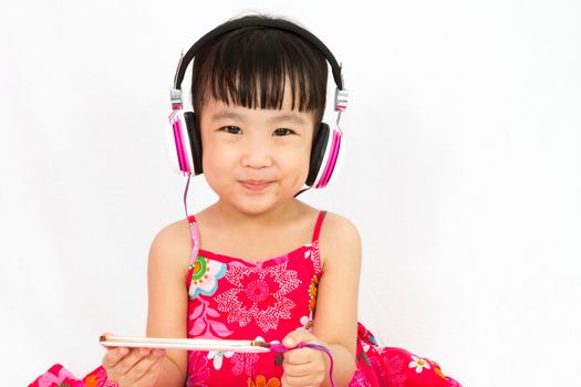 Chinese little girl on headphones holding mobile phone in plain isolated white background.