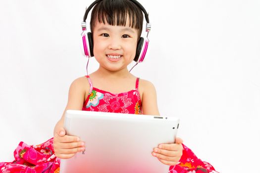 Chinese little girl on headphones holding tablet in plain isolated white background.