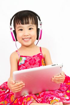 Chinese little girl on headphones holding tablet in plain isolated white background.